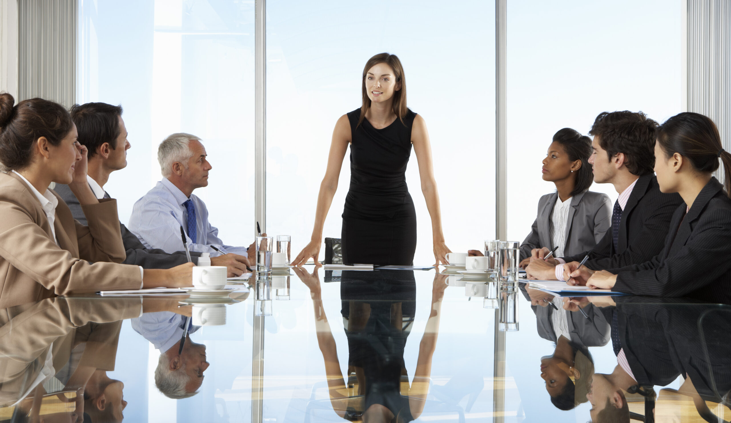 The photo shows a woman standing as a leader at a meeting with staff.